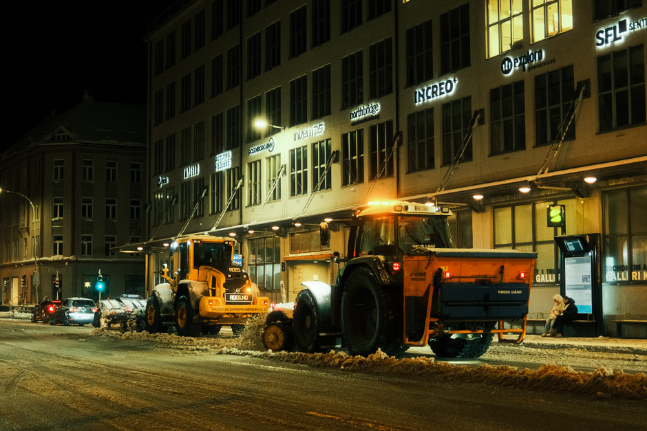 A yellow forklift truck is positioned on a paved surface outside a large industrial warehouse with a corrugated metal exterior painted in shades of blue and grey. The forklift is lifting or preparing