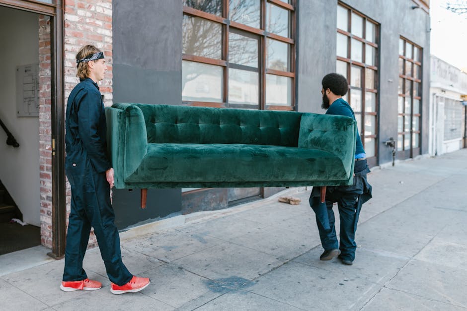 Two movers are outside a building on Westow Hill during a furniture transport process as part of a home relocation service by storagecrystalpalace.com. One mover, wearing a blue jacket and red sneaker